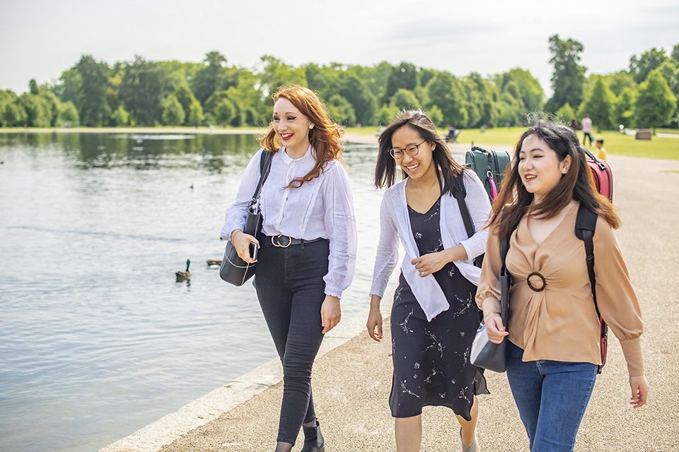 Three students walking in park past lake